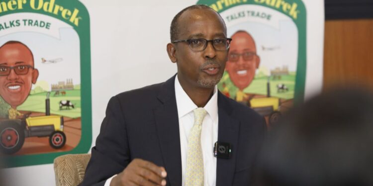 Odrek Rwabwogo, flanked by reporters, discusses his new radio and podcast series, "Farmer Odrek Talks Trade," aimed at empowering Ugandan farmers with practical knowledge to improve production and exports.